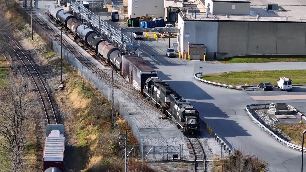 Aerial view of American industrial area with freight train riding through processing facility, showing rail infrastructure, storage tanks and large utility buildings in daylight. Lititz , PA