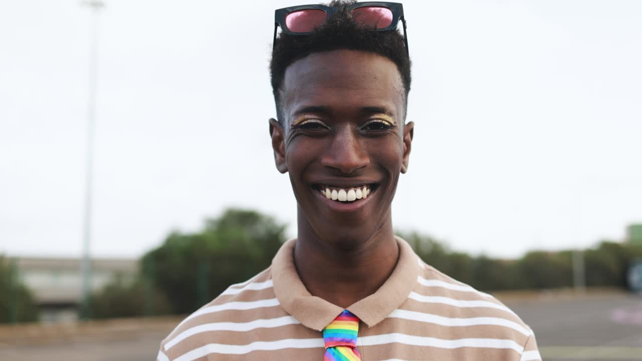 Uomo africano gay felice e truccato che sorride in camera all'aperto.