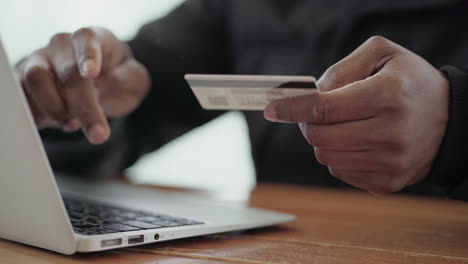 afro-american middle-aged male hand buying goods from internet on laptop with credit card