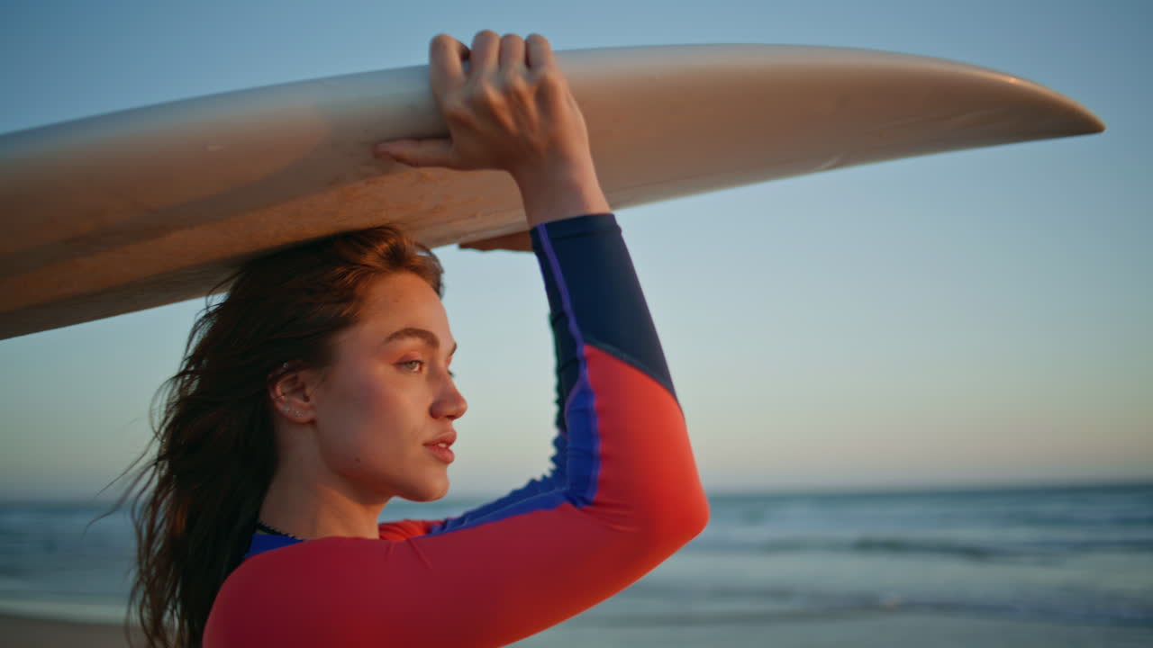 Sunset sportswoman carrying surfboard at beach portrait. Girl turning camera
