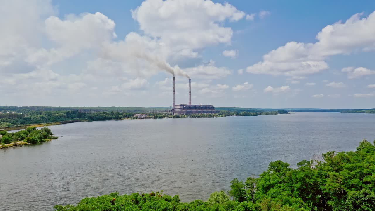 River view from above and two pipes of factory plant. Smoke from the pipes of power plant station at the bank of a river in summer. Aerial view.