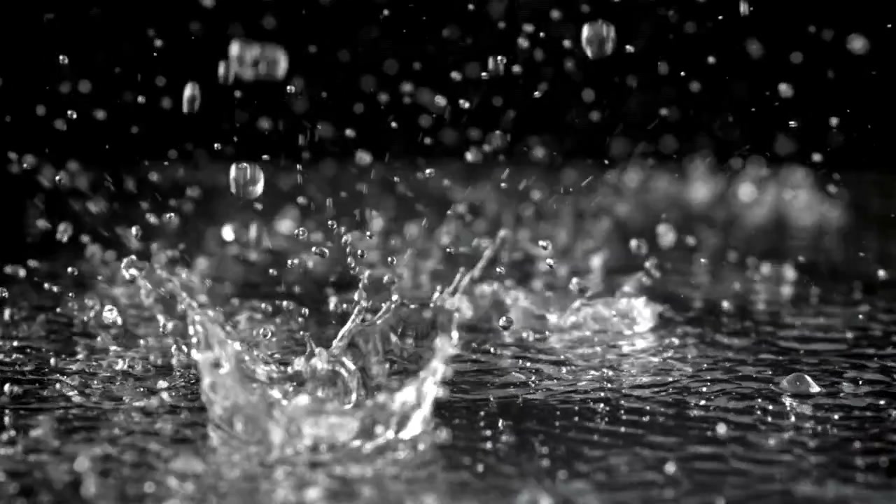 暗い背景の水面に雨粒が飛び散るスローモーション