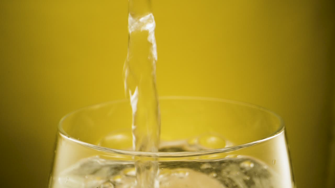 Riempire un bicchiere con acqua frizzante, sfondo giallo