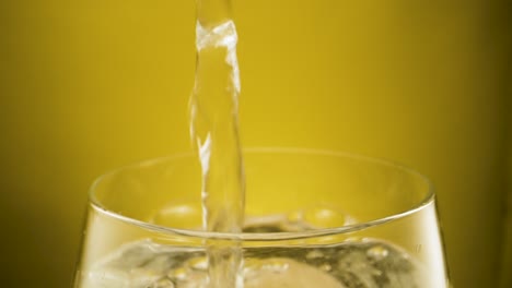 Filling-glass-with-sparkling-water,-yellow-background