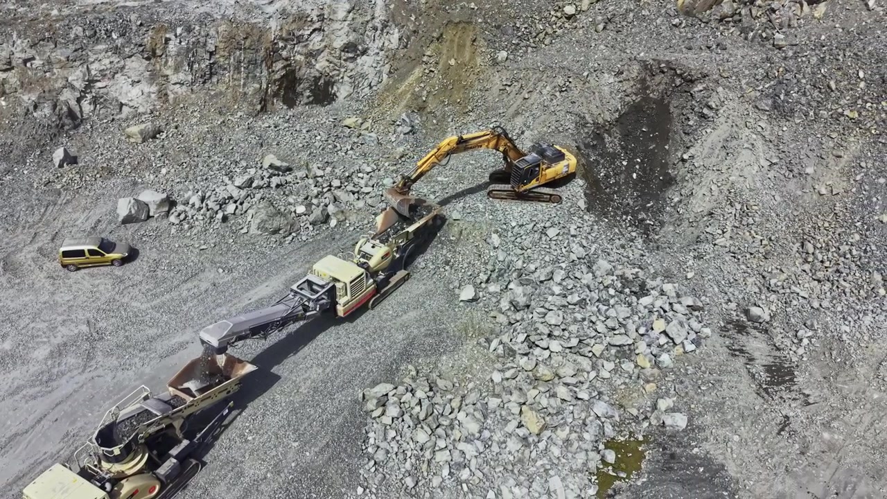 Work takes place in granite quarry with heavy machinery moving rocks and minerals during daytime