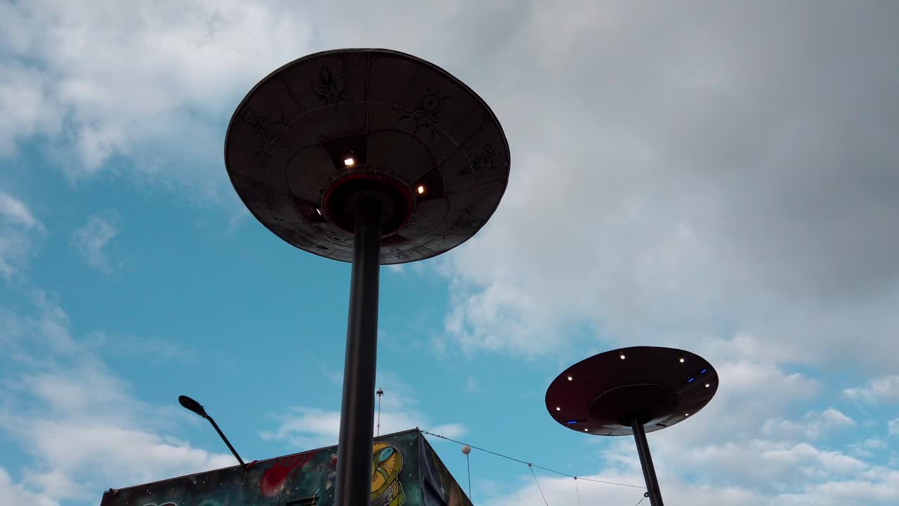 Semi orbit view of a flying saucer-shaped lamp at Museo OVNI, captured from below under a cloudy blue sky in Mexico