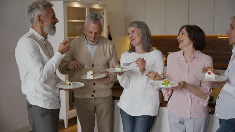 Group-Of-Cheerful-Senior-Friends-Chatting-And-Eating-A-Delicious-Dessert,-Standing-In-A-Modern-Style-Kitchen-1