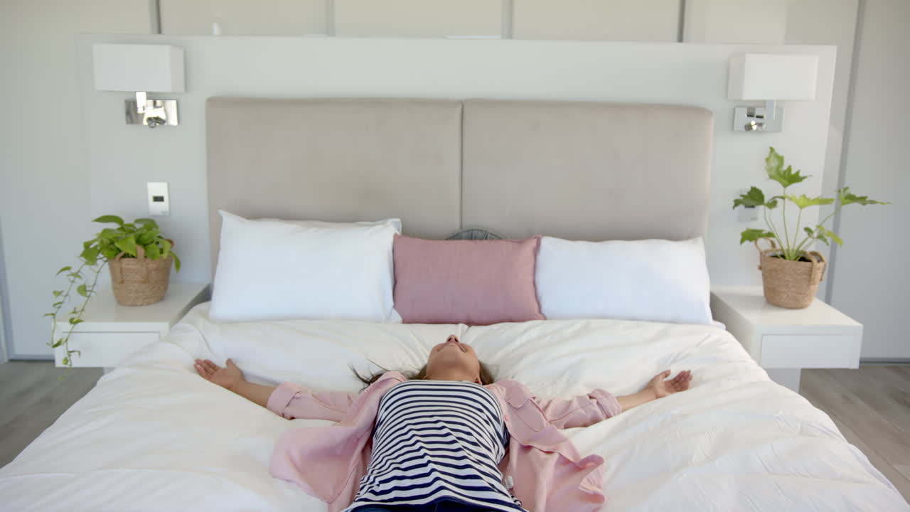 Relaxing on bed, woman lying down with arms outstretched in bedroom