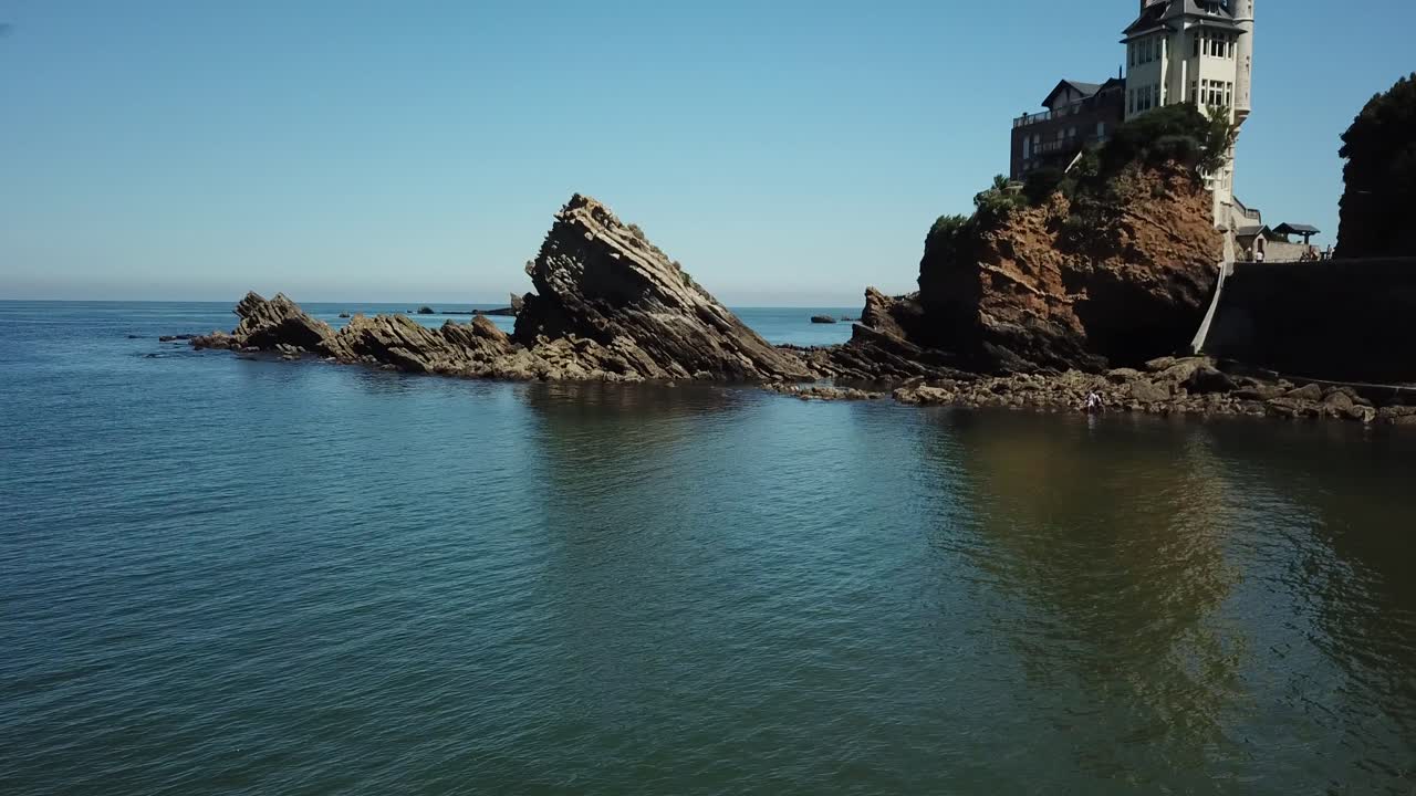 drone volando bajo sobre el mar con un hermoso edificio de lujo encaramado en el fondo de la playa de biarritz, francia