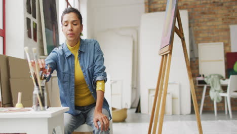 mujer biracial selecciona pinceles en un estudio brillante