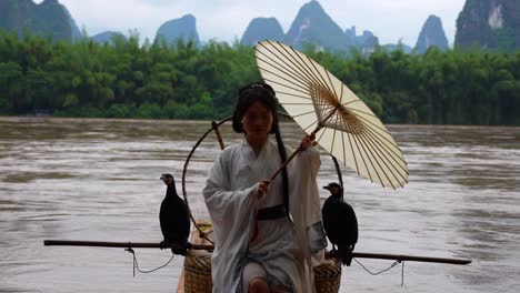 Hanfu-Mädchen-Sitzt-Auf-Einem-Bambusfloß-Und-Hält-Einen-Regenschirm,-Während-Sie-Ihr-Haar-Richtet