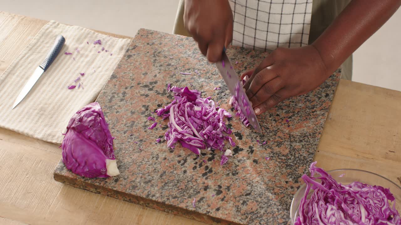 African American man placing half cabbage for slaw, steadying, chopping with chef knife on granite