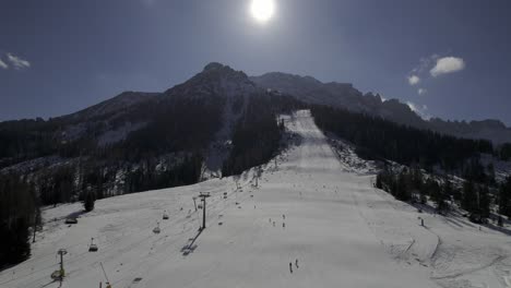 Drone-shot-at-Carezza-Ski-Resort-in-winter,-showing-the-snow-covered-Pra-dei-Tori-slope-as-skiers-carve-their-way-down