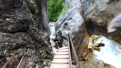 smooth pov footage of someone walking down wooden stairs between two rocks, next to a wild white river in a beautiful canyon