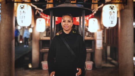 una mujer está orando en un santuario japonés por la noche, rodeada de linternas tradicionales que crean una atmósfera serena y espiritual.