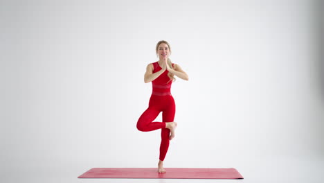 A-woman-in-a-red-tracksuit-looking-into-the-camera-conducts-training-and-tells-and-shows-exercises-from-yoga-or-Pilates-on-a-white-background.-Yoga-instructor-shows-exercises-for-home-classes