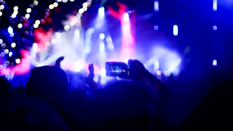 abstract silhouette people in a crowd with hands up, dancing and holding smart phones. lots of flashes of light and out of focus light bulbs.