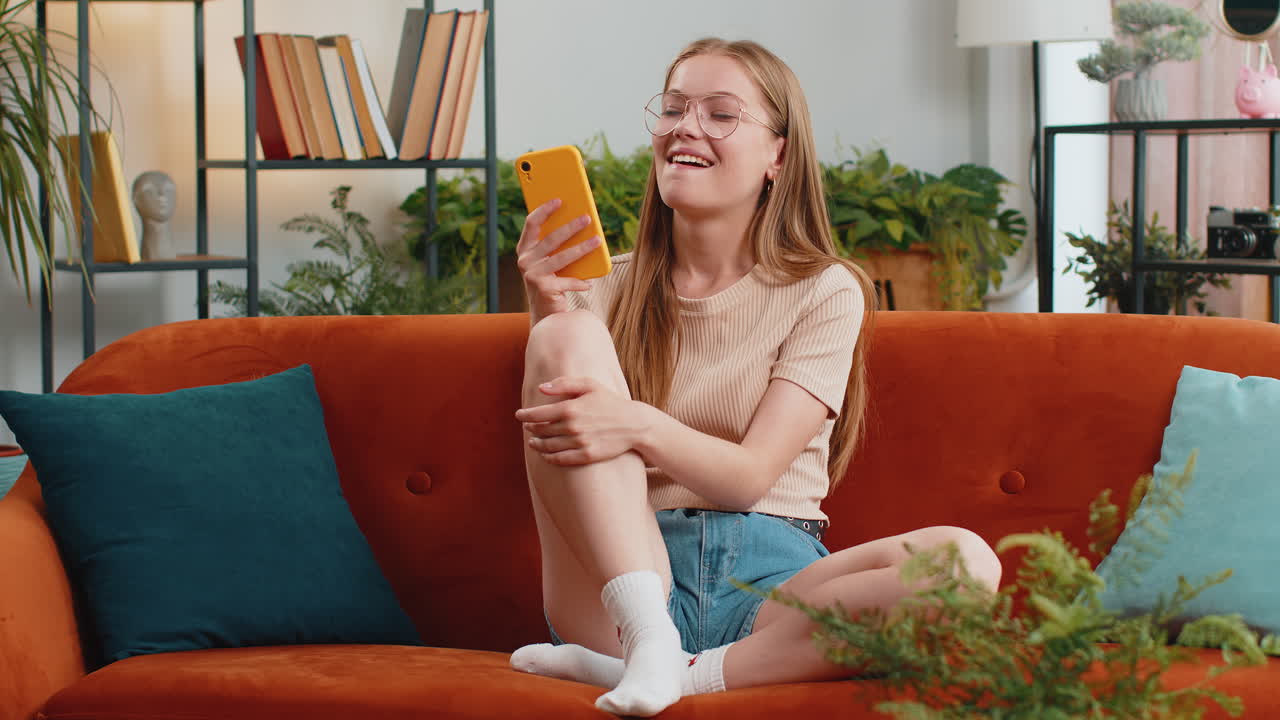 mujer sentada en el sofá usando un teléfono inteligente compartiendo mensajes en aplicaciones de redes sociales viendo películas