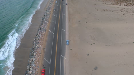 aerial drone shot of pacific coast highway, ocean waves while following fast cars