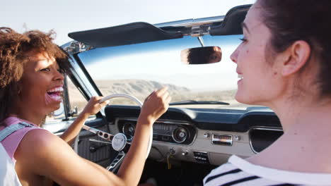 two female friends driving on a desert road in a classic car