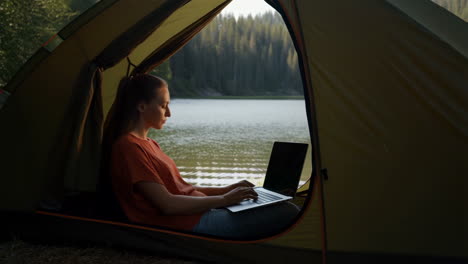woman working on laptop in tent by the lake