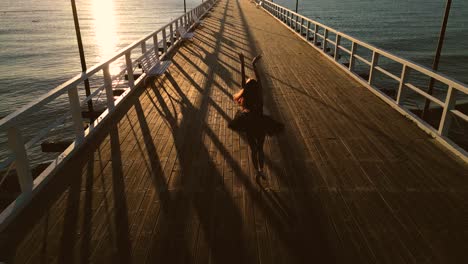 bailarina expresando pasos de ballet en el muelle de la playa al atardecer