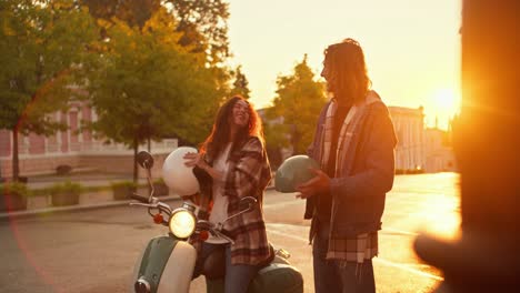 a girl and a guy, brunettes in checkered shirts, take off their protective helmets for riding a moped, hug and rejoice at sunrise on the street. happy couple guy and girl take off their protective helmets, straighten their hair and communicate