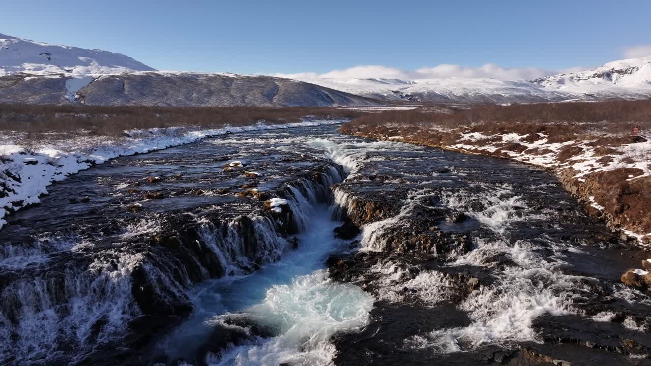 Brúarfoss waterfall in Iceland cascades over rugged volcanic rock, creating mesmerizing turquoise waters framed by a winter landscape.