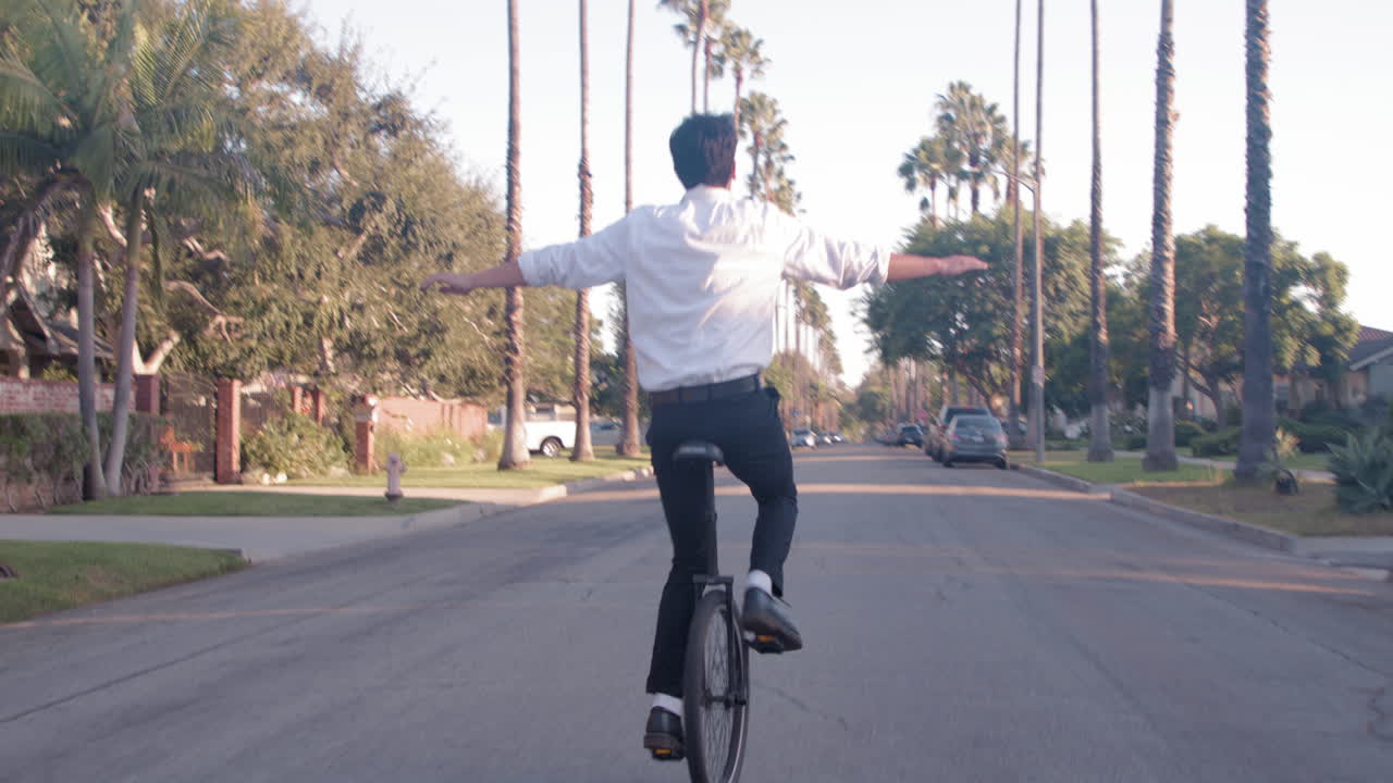 Man riding a unicycle on a palm tree lined street