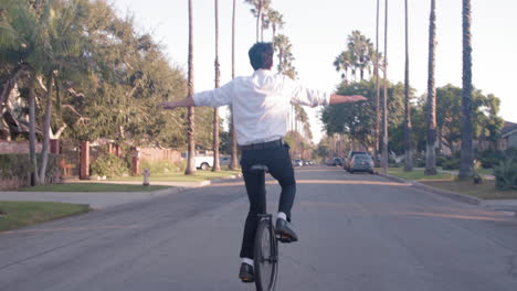 man riding a unicycle on a palm tree lined street