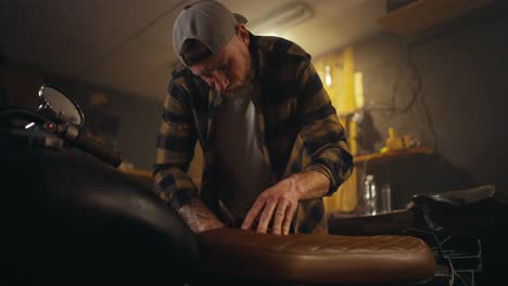 confident male mechanic in a checkered shirt is repairing a motorcycle and selecting the necessary spare parts in his workshop studio