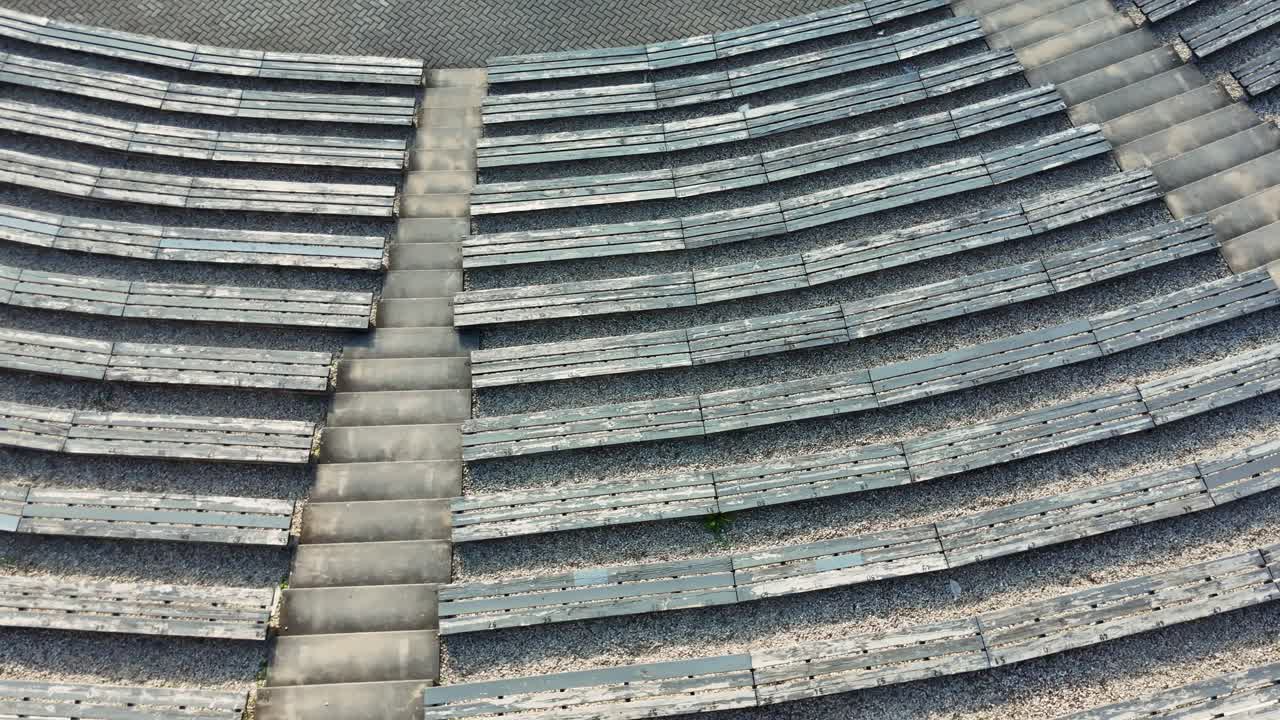 Overhead perspective spinning and revealing wooden benches and concrete stairs curving elegantly at Sauleskalns open air theatre, nestled in Latvian summer landscape