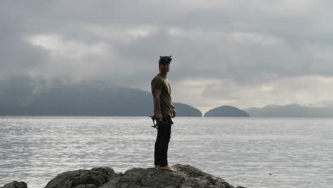 caucasian man with fpv quadcopter standing on rock overlooking calm sea with overcast