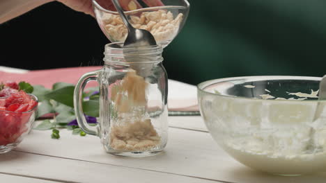 assembling dessert - filling jar with crushed crackers using a spoon and shaking gently to spread evenly