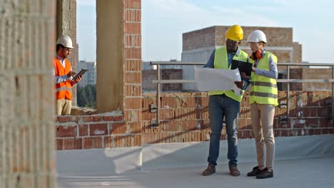 multiethnic young man and woman workers at the building site disputing some problems and issues with drafts and tablet computer. outdoor.