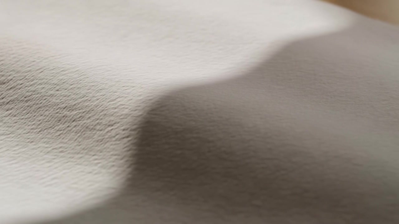Tessuto testurizzato beige che si sposta al variare della luce, le ombre delle pieghe si scuriscono e rivelano un primo piano della trama.