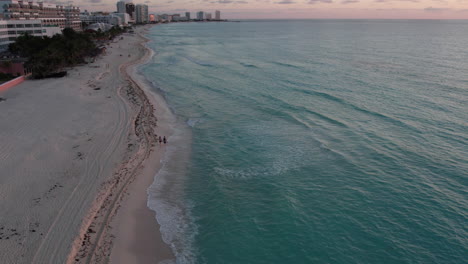 vista de drones siguiendo a una pareja caminando en la playa de arena blanca al atardecer, cancún, méxico