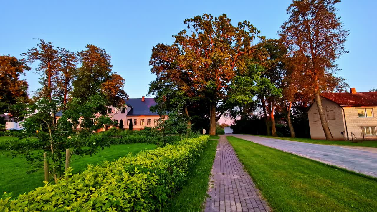 Small village houses with trees and sidewalk under warm evening sunlight in Latvia