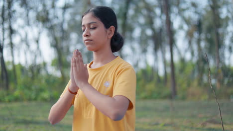 close up shot of a slim young woman doing prayer pose with closed eyes in the forest during sunrise.