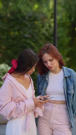 two young women looking at a smartphone outdoors