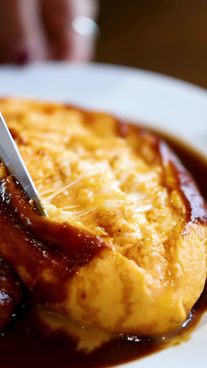 En kniv skjærer omurice, og avslører et kremet eggefyll ved siden av en hamburgstek i en rik demi-glace saus.