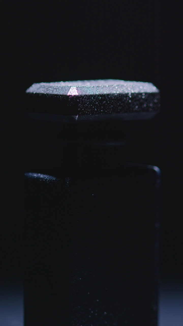 primer plano de una botella de perfume negra con gotas de agua en la tapa en forma de diamante, en condiciones de poca luz