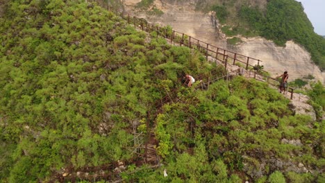 Tourist-walking-down-the-stairs-overgrown-with-tropical-bushes,-aerial-dolly-out-shot