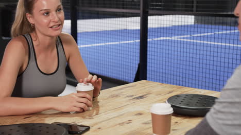 man sitting at table with coffee cup, relaxing after padel tennis match, at indoor court