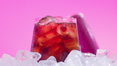 Nahaufnahme-Eines-Gekühlten-Kaltgetränks-Im-Glas,-Das-Aus-Der-Dose-Auf-Eiswürfel-Vor-Rosa-Hintergrund-Gegossen-Wird