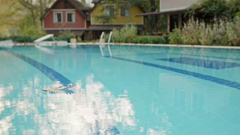 Wide-Shot-of-Fallen-Dried-Leaf-Wandering-in-Swimming-Pool-of-Luxurious-Holiday-Resort-with-Blowing-Wind-in-slowmo