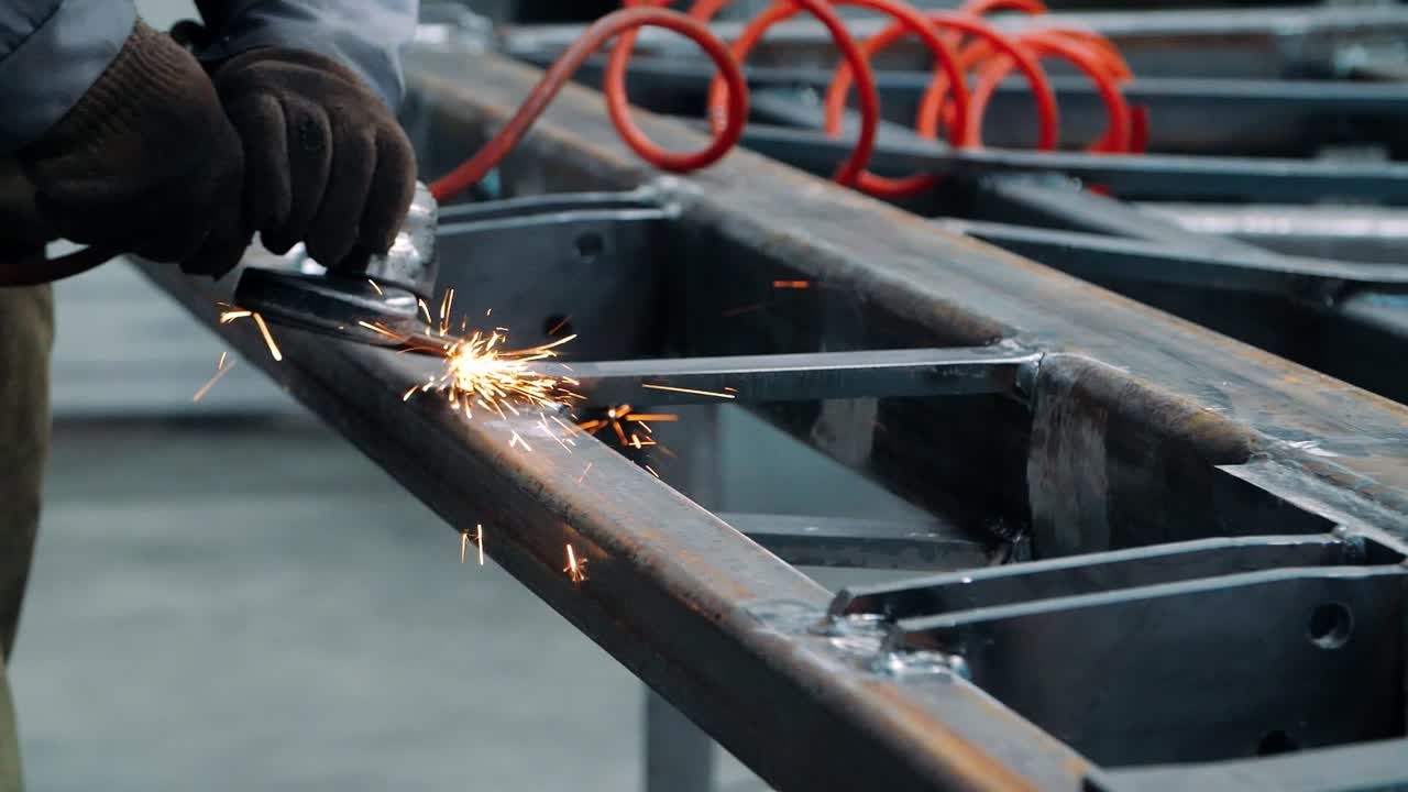 Hombre trabajando con una amoladora eléctrica en una estructura de acero en la fábrica.