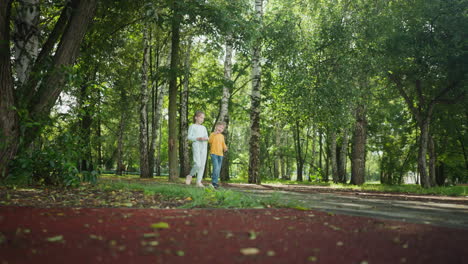 young girl and boy walk side by side along forested park path covered in shade and sunlight, enjoying peaceful nature together as siblings bond during relaxing outdoor stroll in lush natural scenery