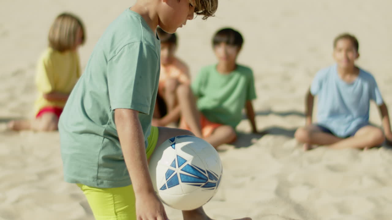 movimiento lento de un niño pateando una pelota de fútbol con los pies en la playa