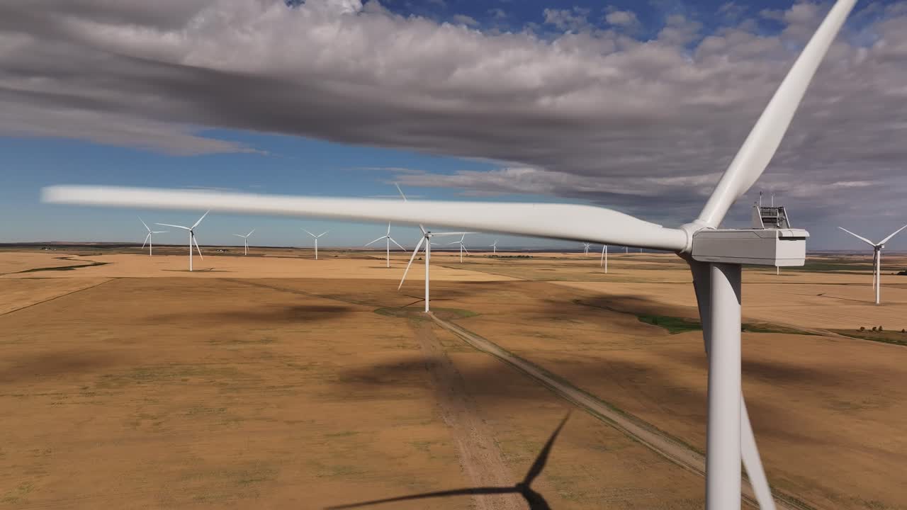 A drone flies backwards from a windmill on a southern Alberta, Canada windfarm